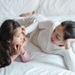 photo of woman and girl talking while lying on bed